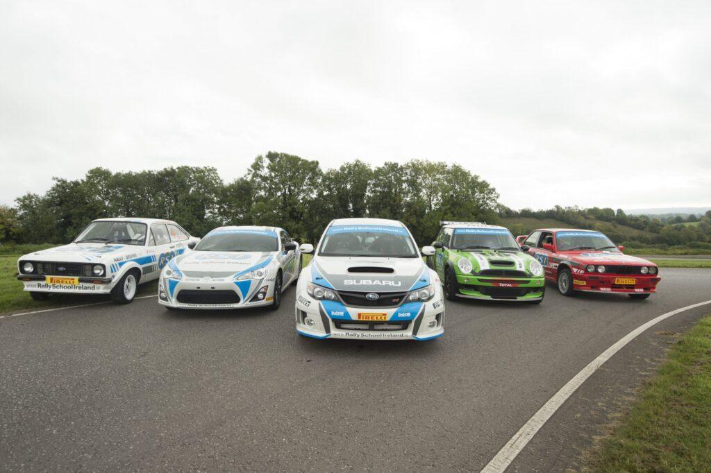 Five rally cars lined up on a track, representing Rally School Ireland with trees in the background.