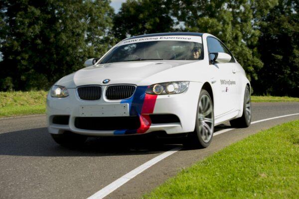 White BMW on a track, showcasing speed and performance during a driving experience event on a sunny day.