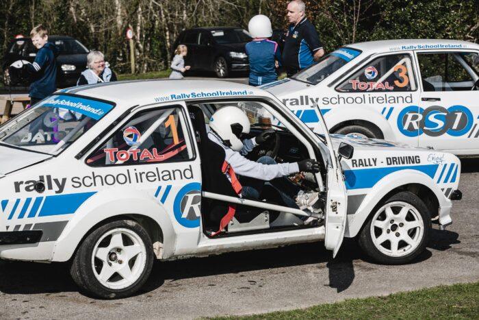 Rally School Ireland driver preparing in car for track experience, with branded vehicles in background.