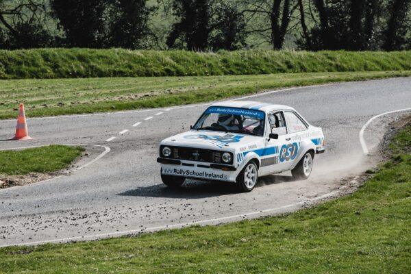 Rally car speeding through a curved track at Rally School Ireland, kicking up dust and navigating a sharp turn.