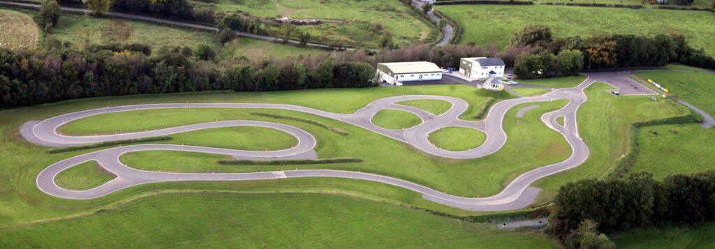 Aerial view of a winding go-kart racetrack surrounded by lush green fields and buildings.