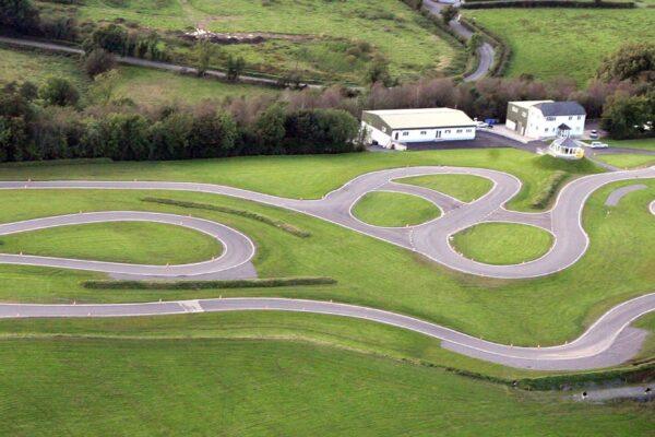 Aerial view of a winding go-kart racetrack surrounded by lush green fields and buildings.