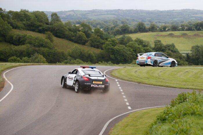 Police car and rally car on scenic countryside road curve.