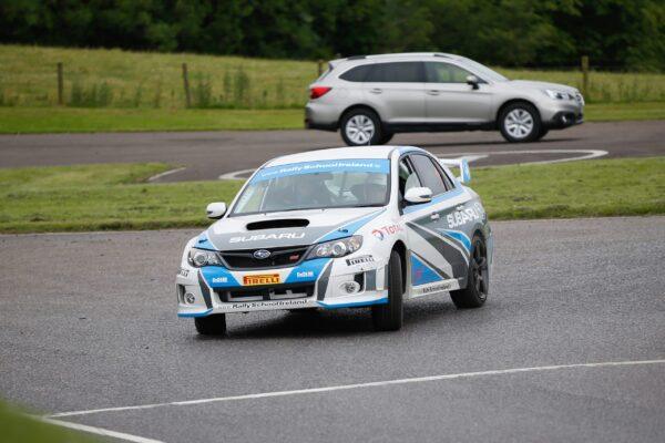 Subaru rally car on track at high speed, showcasing dynamic motion and performance, with grassy background.