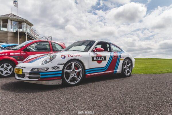 White rally car parked on track with colorful stripes, Pirelli tires, overcast sky in the background.