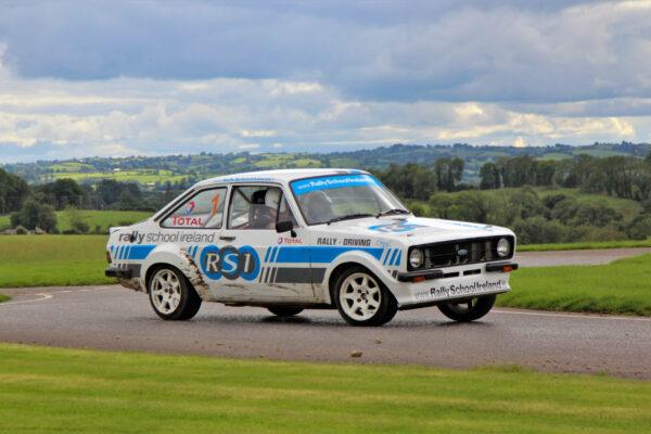 Classic rally car in action on a scenic countryside road, Rally School Ireland branding visible.
