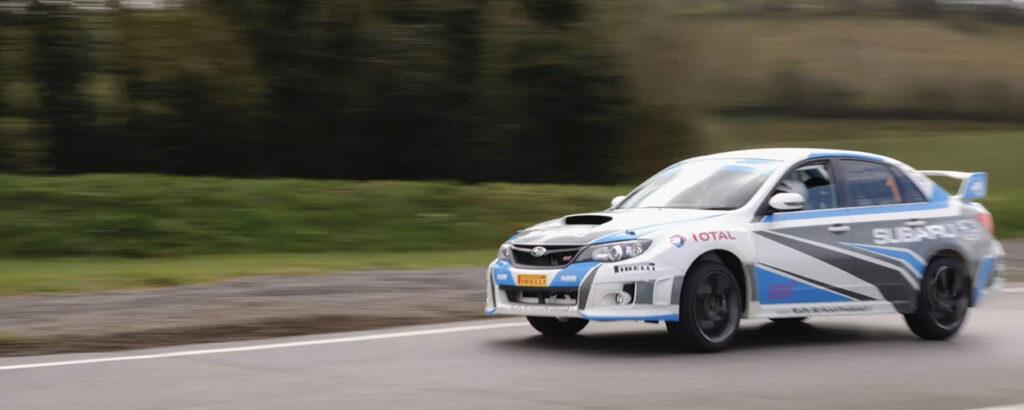 Rally car speeding on a track, showcasing dynamic motion against a blurred green background.