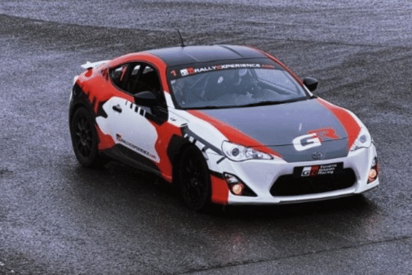 Red and black rally car on wet tarmac, with GR branding, showcasing sporty design and performance.